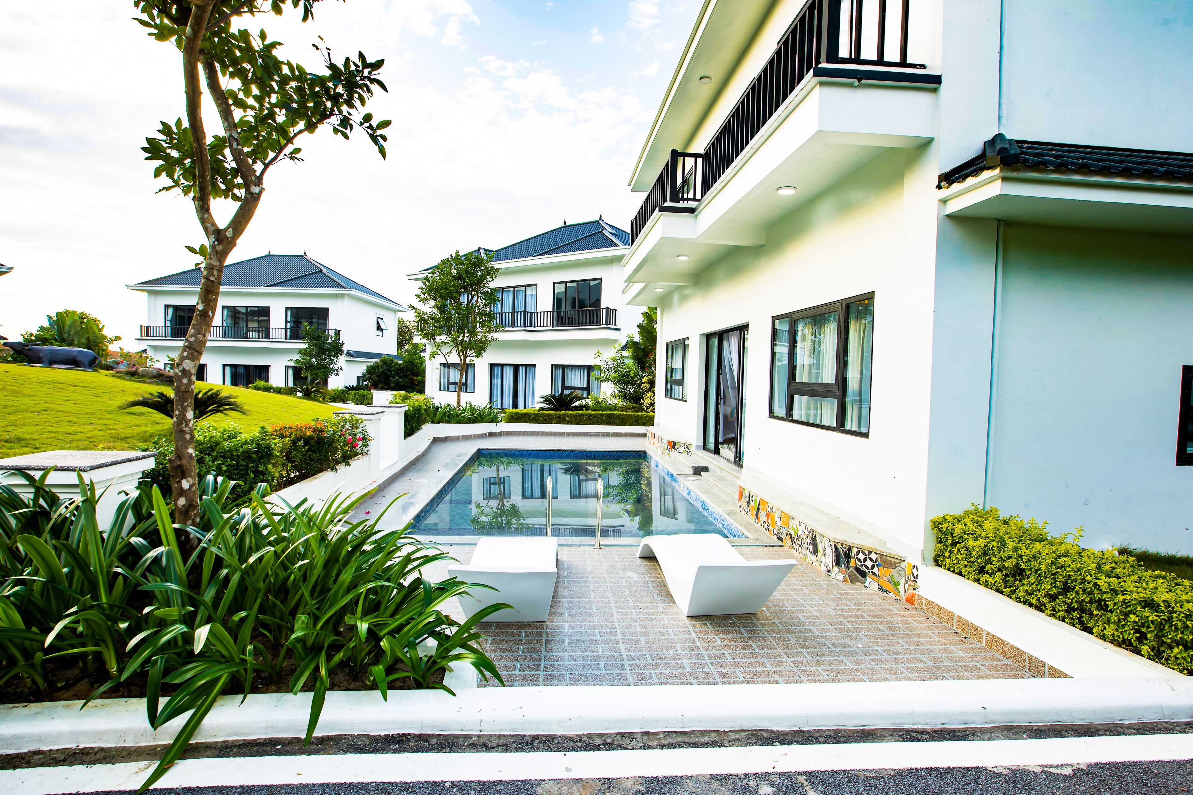 A modern residential building with a swimming pool, multiple balconies, and lush greenery.