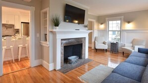 Una sala de estar moderna con chimenea, un televisor de pantalla plana montado encima y una zona de estar con sofá y sillones.