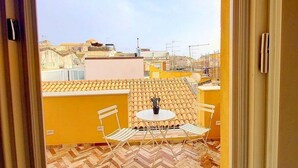 A balcony with a tiled floor, a small table with two chairs, and a view of the cityscape. - Appartamento Coturnia: A characteristic and welcoming apartment in the heart of the fascinating island of Ortigia, with Free WI-FI. (Siracusa)