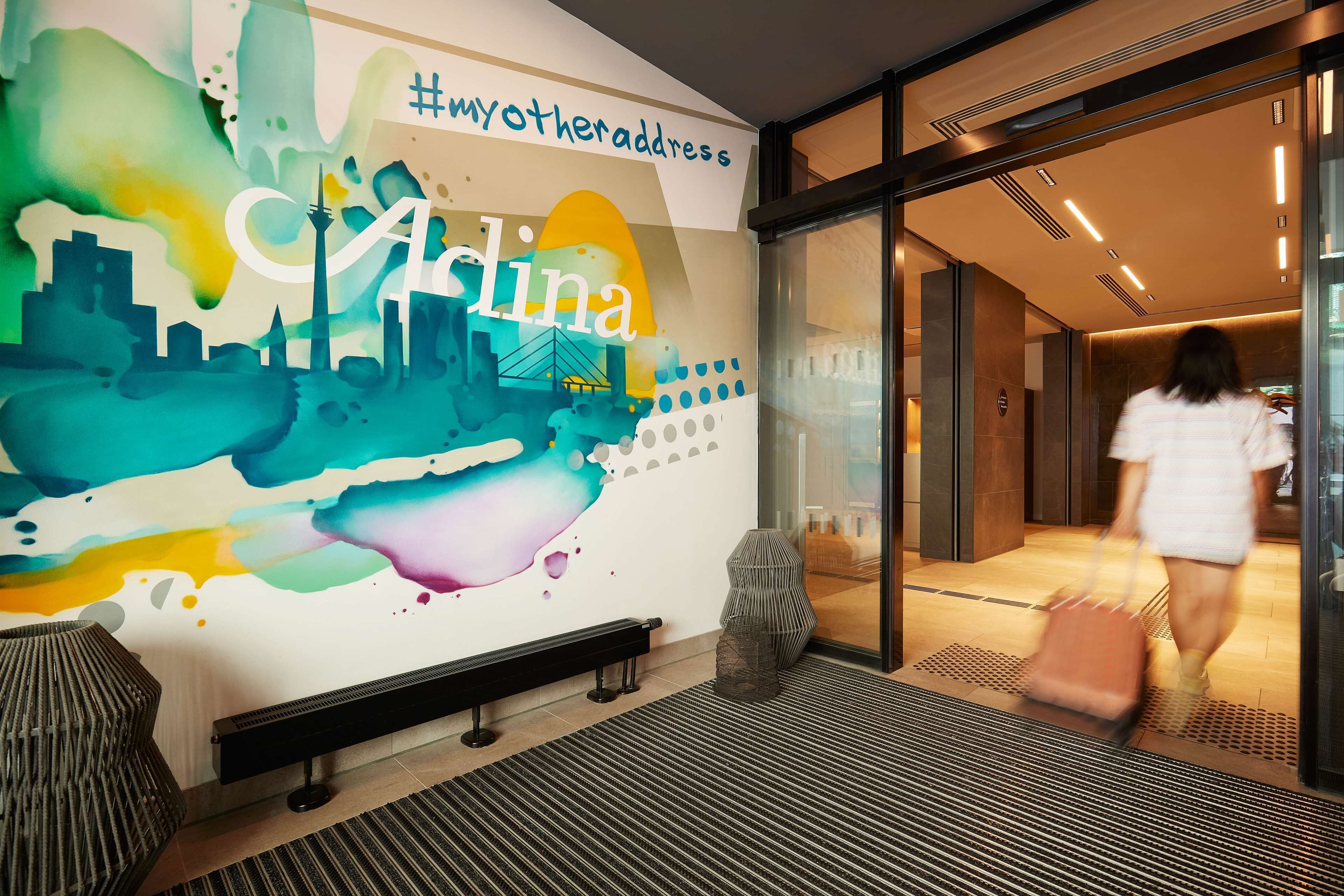 Una entrada de hotel moderna con un mural colorido, un banco y una puerta de cristal.