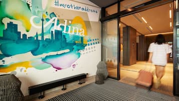 A modern hotel entrance with a colorful mural, a bench, and a glass door.