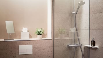 Un baño moderno con cabina de ducha de vidrio, una planta en maceta, una caja de pañuelos y una botella de champú en un estante.