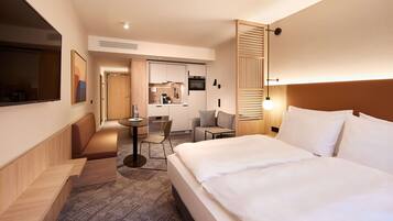 Een hotelkamer met een groot bed, een bureau, een stoel, een bank en een kitchenette op de achtergrond.
