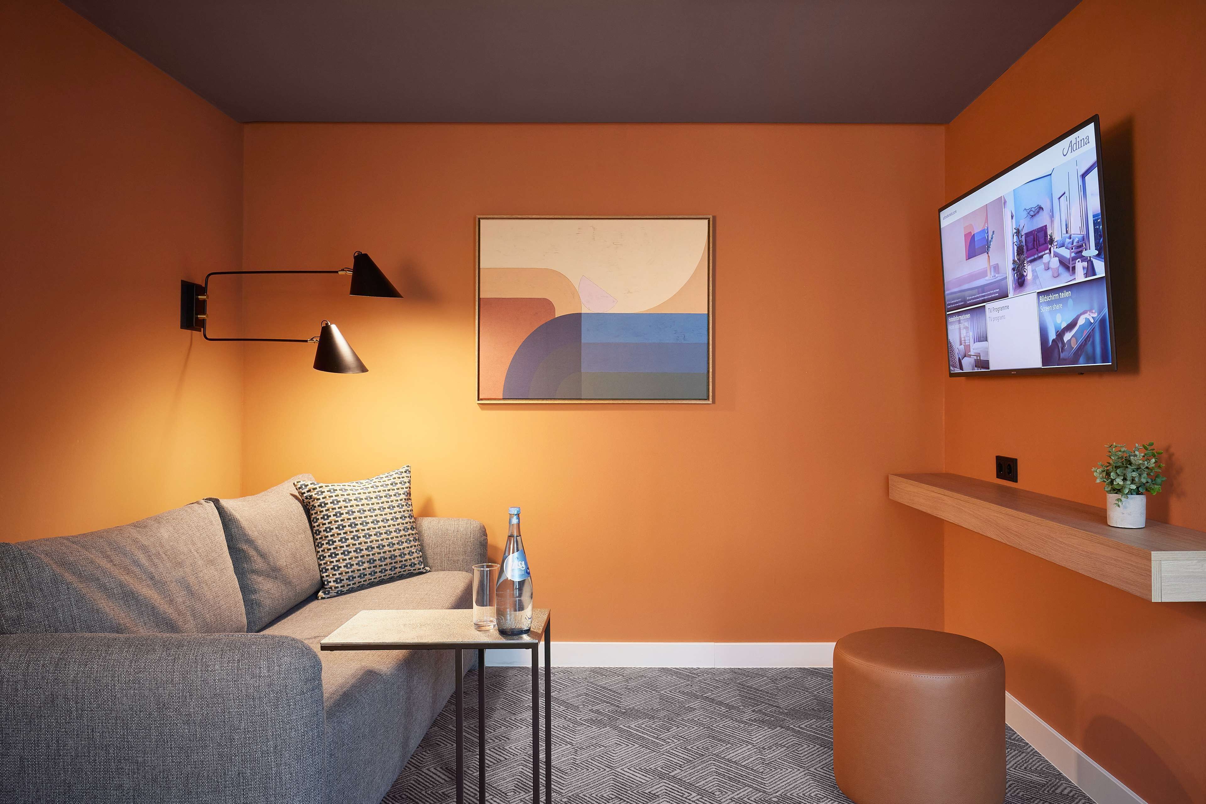 Een moderne kamer met een bank, een kleine tafel met een fles en glazen, een wandtelevisie en een plank met een plant.