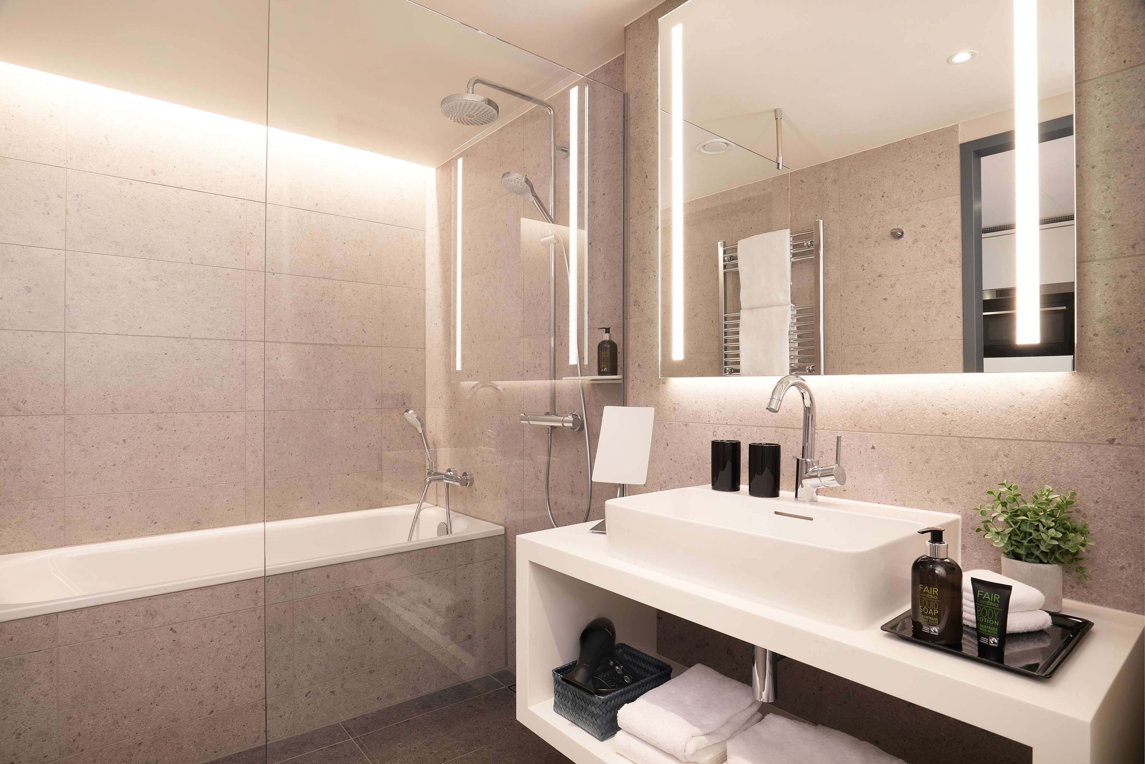A modern bathroom with a large bathtub, a sink with a mirror, and a shelf with toiletries.