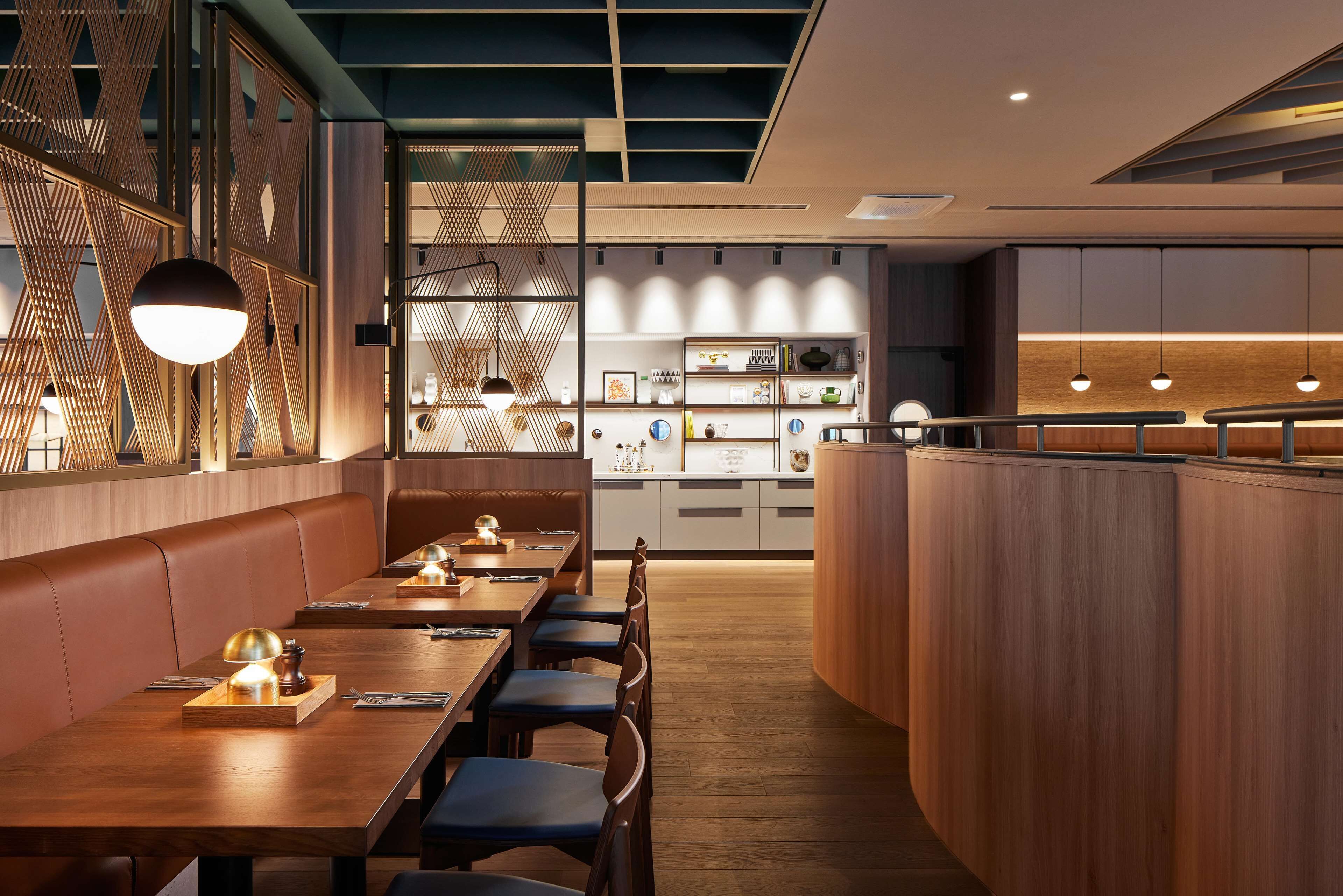 Un restaurant moderne avec des tables en bois, des banquettes confortables et des luminaires suspendus.