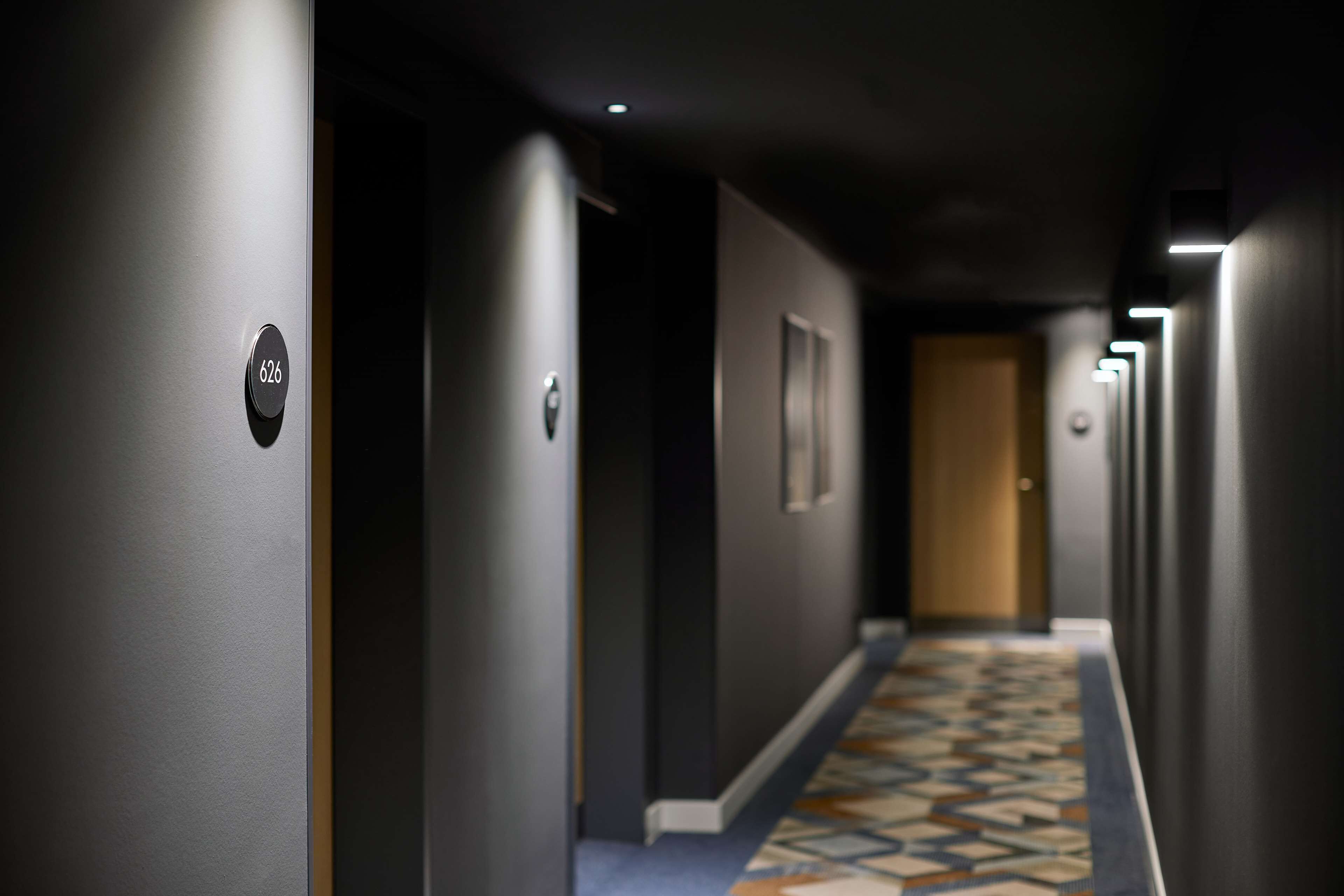 Een hotelgang met vloerbedekking, een deur aan het einde en een nummerbord aan de muur.