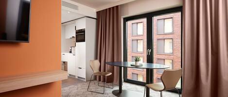 A modern hotel room with a round table, two chairs, a TV on the wall, and a large window with curtains.
