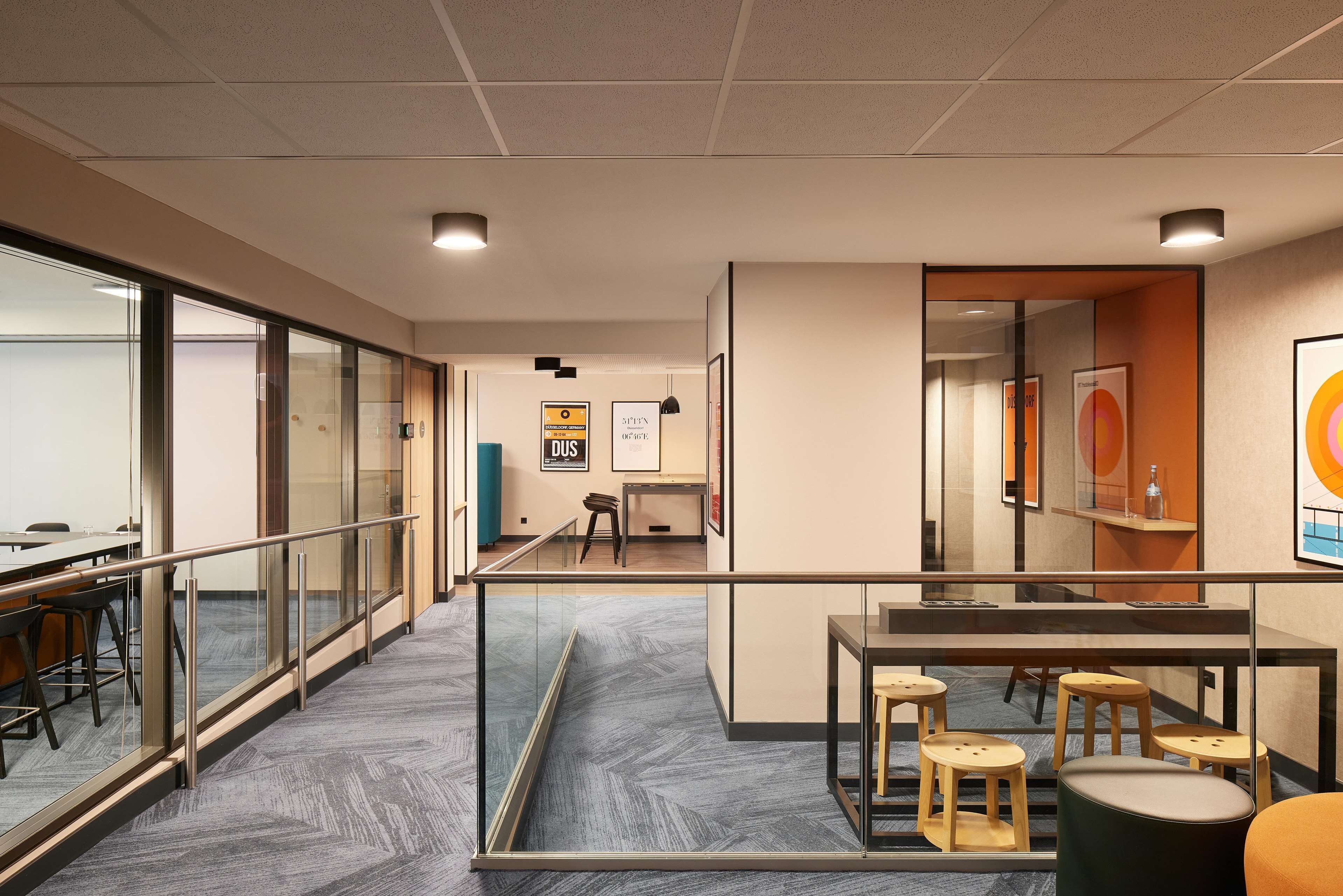 Un espacio de oficina moderno con separaciones de vidrio, un entrepiso con asientos y una escalera visible.