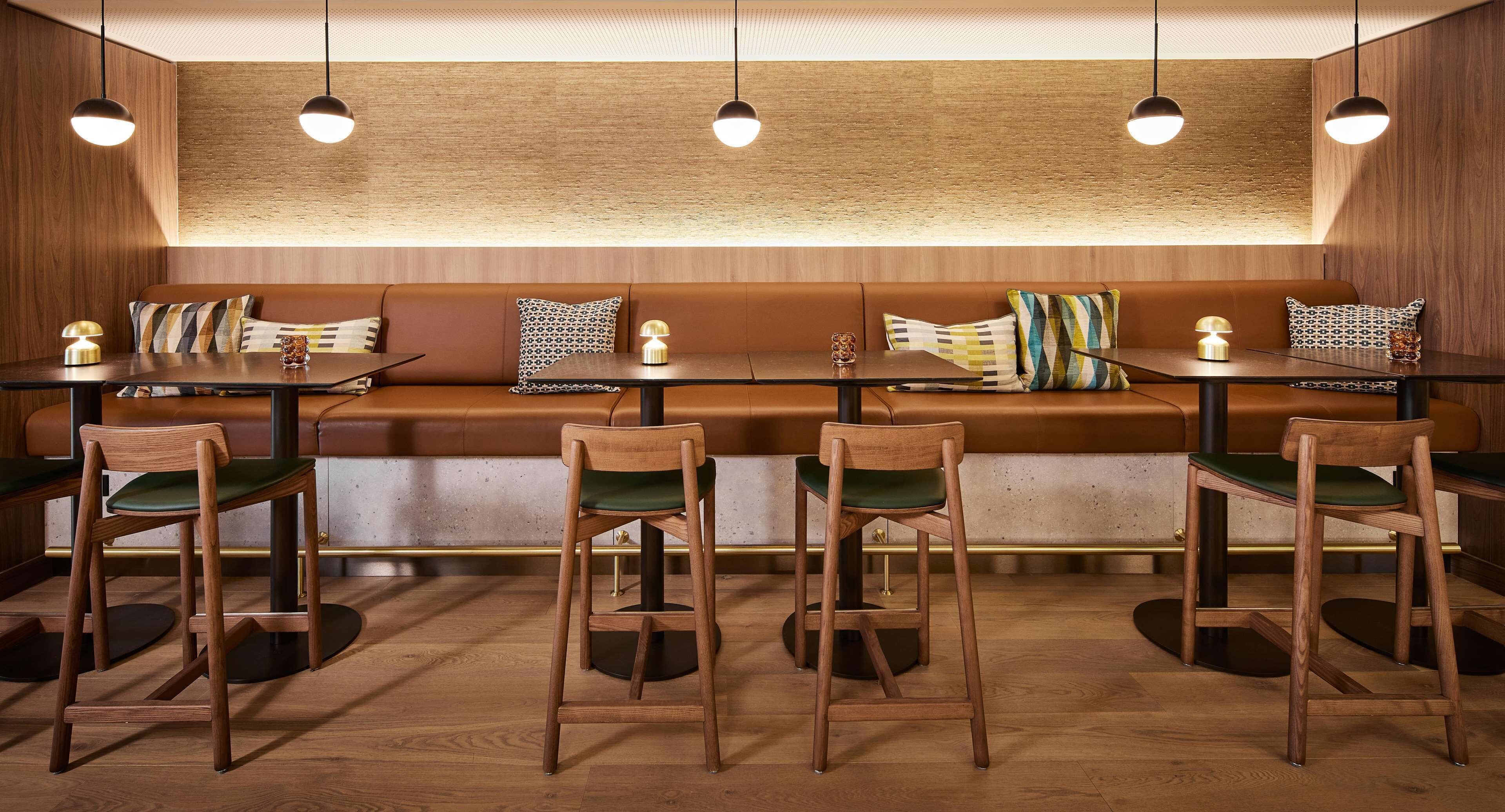 Interior de restaurante con cabinas de madera, sillas con asientos acolchados en verde e iluminación colgante.