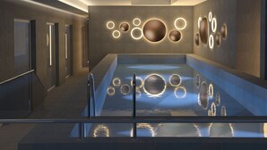 A modern spa area with a large, rectangular hot tub, a wall with circular light fixtures, and a wooden floor.