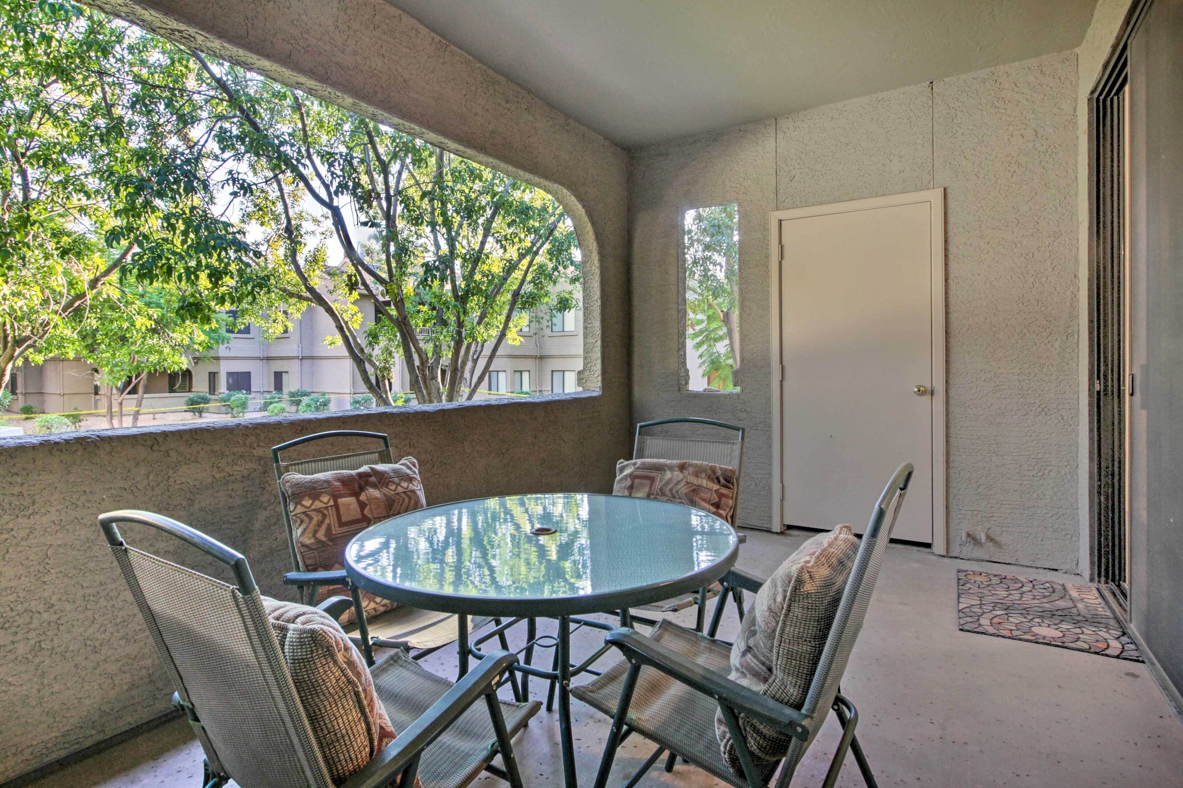 A round table with chairs in a covered outdoor area with a view of trees and buildings.