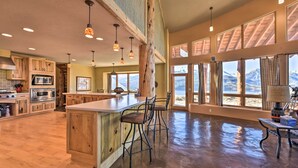 Une cuisine spacieuse dotée de meubles en bois, d’un grand îlot central avec des tabourets de bar et de grandes fenêtres offrant une vue sur les montagnes.