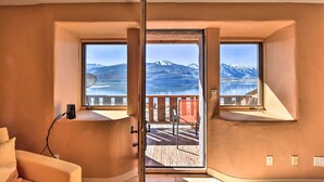 Une pièce dotée d’une grande fenêtre donnant sur un lac et des montagnes. À l’extérieur de la fenêtre, on trouve une terrasse en bois.