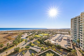 A hotel with a parking lot, palm trees, and a view of the beach.