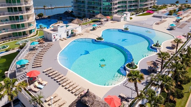 Un complexe hôtelier doté d’une grande piscine centrale, de plusieurs piscines plus petites et d’une variété de chaises longues et de parasols.