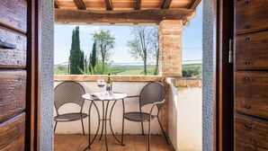 A balcony with a table and two chairs, a bottle of wine, and a view of the countryside. - Independent villa with WIFI, private pool, A/C, close to Cortona! (Castiglion Fiorentino)