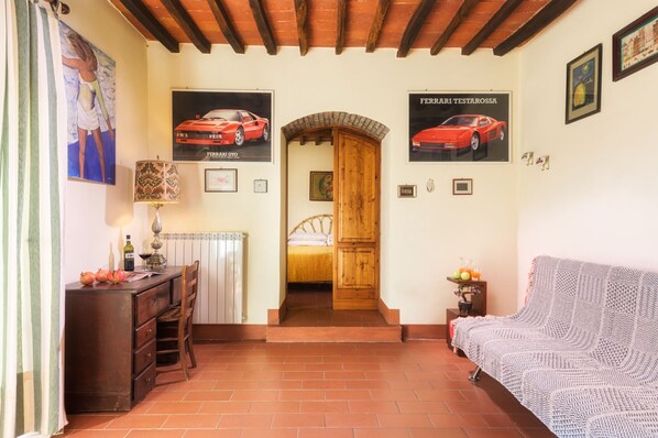 Una habitación con una cama, un armario de madera, una mesa con una lámpara y un sofá. Hay dos cuadros en la pared.