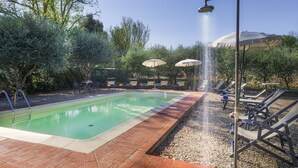 A swimming pool with a brick border, surrounded by lounge chairs and umbrellas, with trees in the background. - Independent villa with WIFI, private pool, A/C, close to Cortona! (Castiglion Fiorentino)
