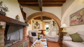 A cozy living room with a brick fireplace, comfortable seating, and a view through an archway. - Independent villa with WIFI, private pool, A/C, close to Cortona! (Castiglion Fiorentino)