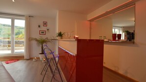 A modern kitchen with a red accent wall, a dining area with a chair, and a large window offering a view of greenery. - Countryside Holiday Home in Stoumont with Terrace, Garden (Stoumont)