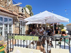 Un área de asientos al aire libre con sombrillas blancas, un edificio de piedra y un letrero que anuncia un restaurante.