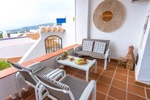 A terrace with a white sofa, a small table, and a decorative wall hanging. - Capuchinos 55 San Juan Capistrano by Casasol (Nerja)