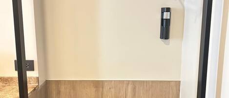 Una habitación minimalista con suelo de madera, una cama con estructura negra, una mesita con bandeja y un perchero.