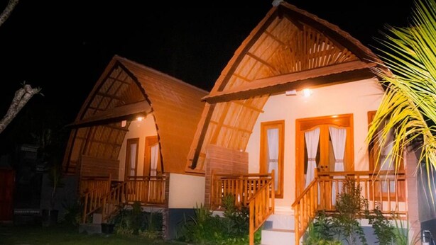 Two wooden cottages with thatched roofs, each with a porch and a staircase leading to the entrance. - Watu Jineng by WizZeLa (Penida Island)