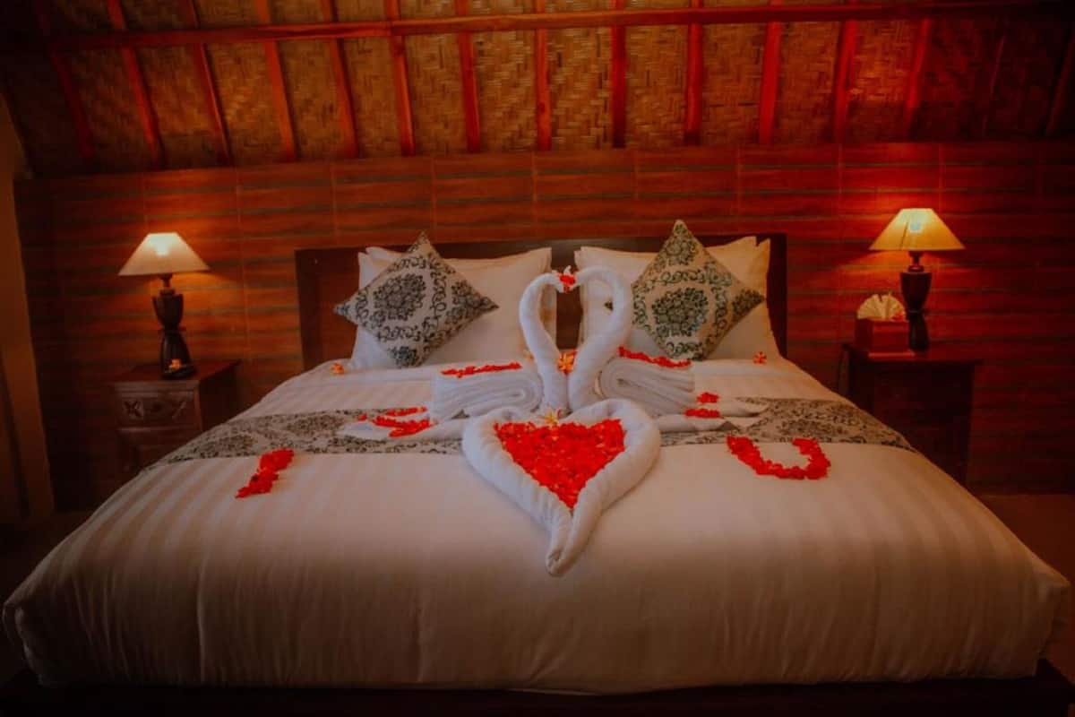 Een bed met een handdoekarrangement in de vorm van een hart en zwanen, aan weerszijden voorzien van nachtkastjes met lampen.
