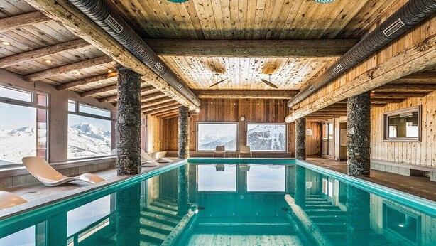 A pool area with wooden beams, stone pillars, and a view of mountains.