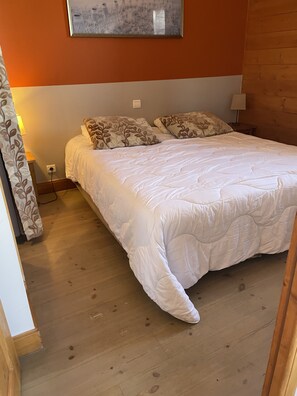 A bedroom with a large bed, a wooden floor, a wall-mounted picture, and a bedside table with a lamp. - Luxury apartment 90m2 sleeps 10 La Plagne Aime 2000 at the foot of the slopes (La plagne)