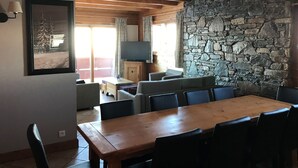 A dining area with a wooden table and chairs, a stone wall, and a television on a wooden cabinet.