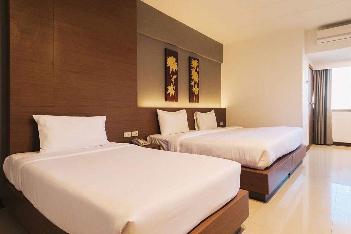 Een hotelkamer met twee bedden, een bureau, een stoel en een groot raam met gordijnen.