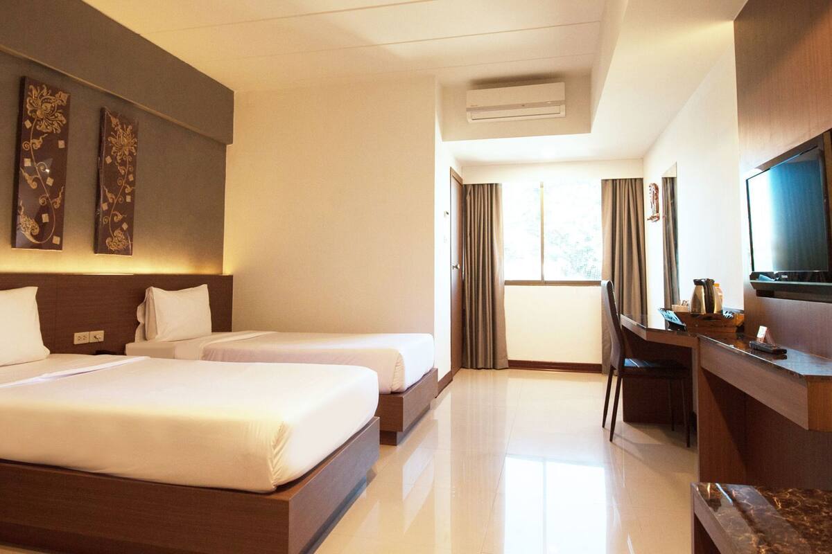 Een hotelkamer met twee bedden, een bureau, een televisie en een raam met gordijnen.