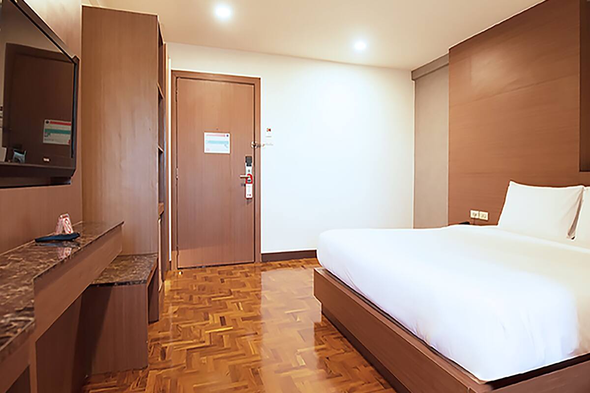 Een hotelkamer met een bed, een houten bureau, een spiegel en een deur.