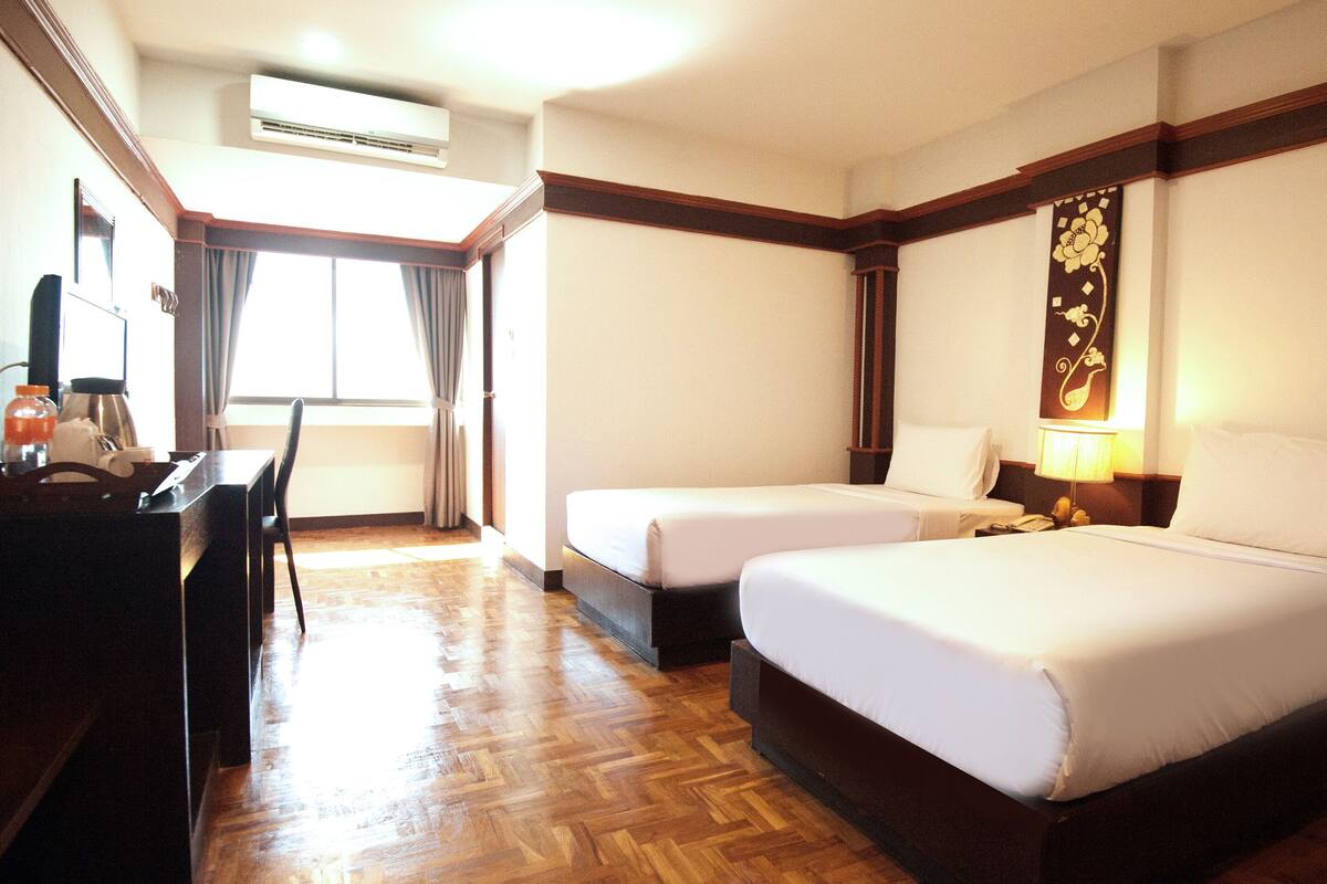 Een hotelkamer met twee bedden, een bureau, een stoel en een raam met gordijnen.