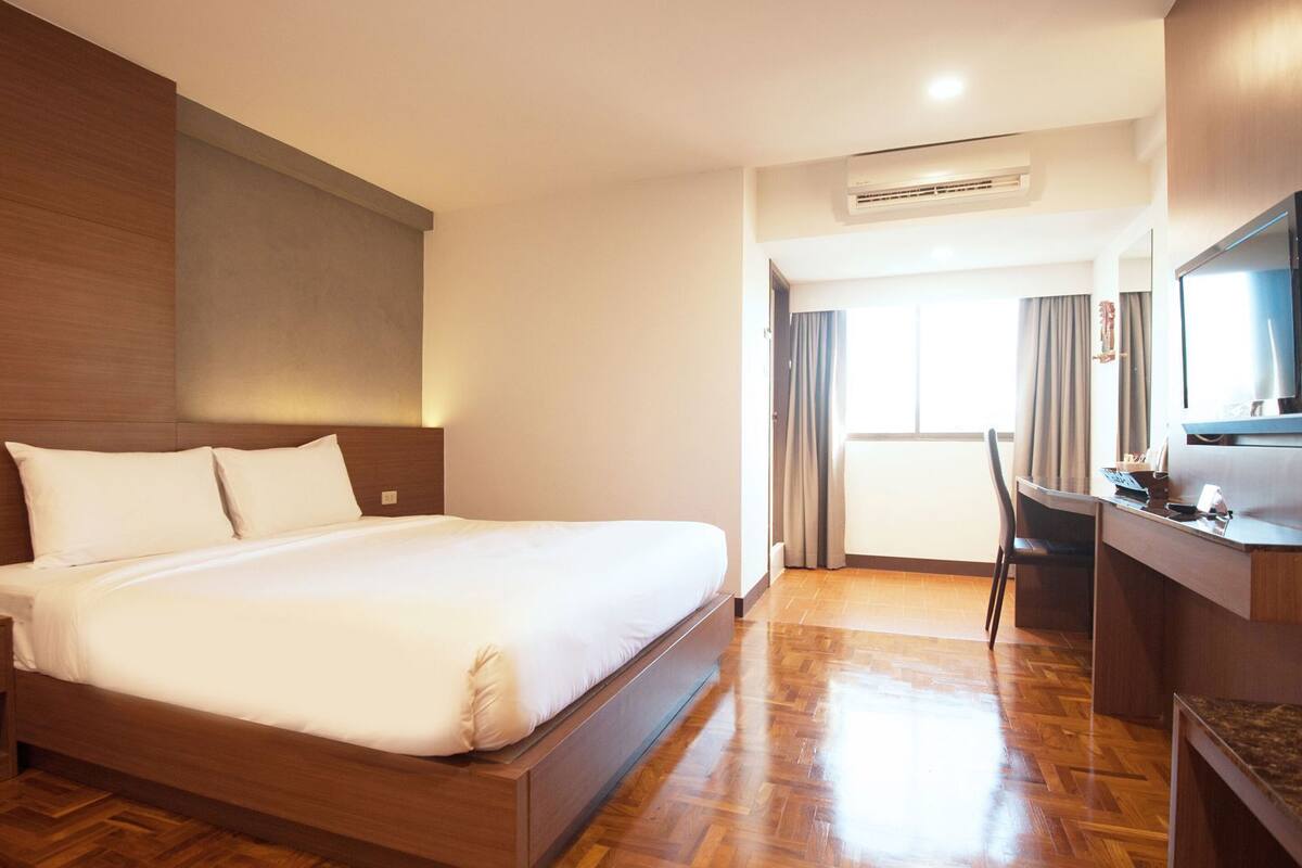 Een hotelkamer met een groot bed, een bureau, een televisie en een airconditioner.
