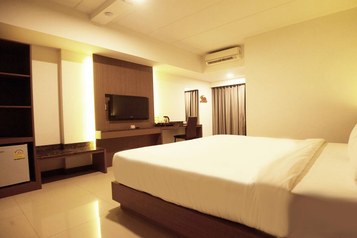 Een hotelkamer met een groot bed, een aan de muur bevestigde televisie, een bureau met een stoel en een minibar.