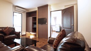 A living room with a leather sofa, a glass coffee table, and a flat-screen TV mounted on a wooden wall. - B2 Chang Phueak Gate Premier Hotel (Chiang Mai)