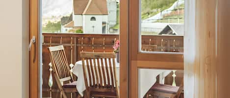 A room with a sliding glass door leading to an outdoor deck with wooden furniture and a view of a mountain and a church.