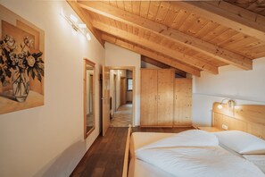 Un dormitorio con techo de madera, cama con ropa de cama blanca, armario de madera y un cuadro en la pared.