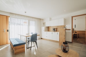 A modern kitchen with white cabinets, a wooden countertop, and a dining area with a bench and chairs.