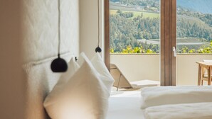 A bedroom with a large window, a bed, a chair, and a view of a landscape.