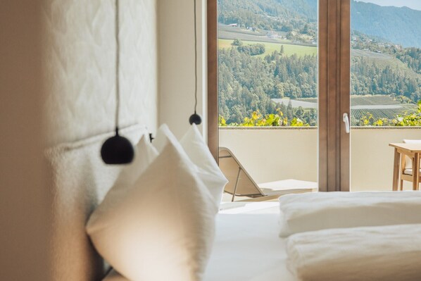 A bedroom with a large window, a bed, a chair, and a view of a landscape.