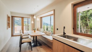 A modern kitchen with a large window, a dining area with a table and chairs, and a built-in bench with cushions.