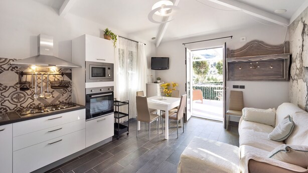Una cocina moderna con estufa, horno y microondas, un comedor con mesa y sillas, y una sala de estar con sofá y televisor.