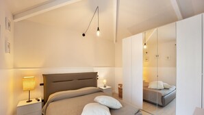 Un dormitorio con una cama, mesitas de noche, una lámpara y un espejo.