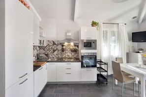 Une cuisine moderne avec des meubles blancs, un four à micro-ondes, un four traditionnel et un coin repas comprenant une table et des chaises.