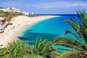 Una playa con agua turquesa cristalina, palmeras y edificios a la izquierda.